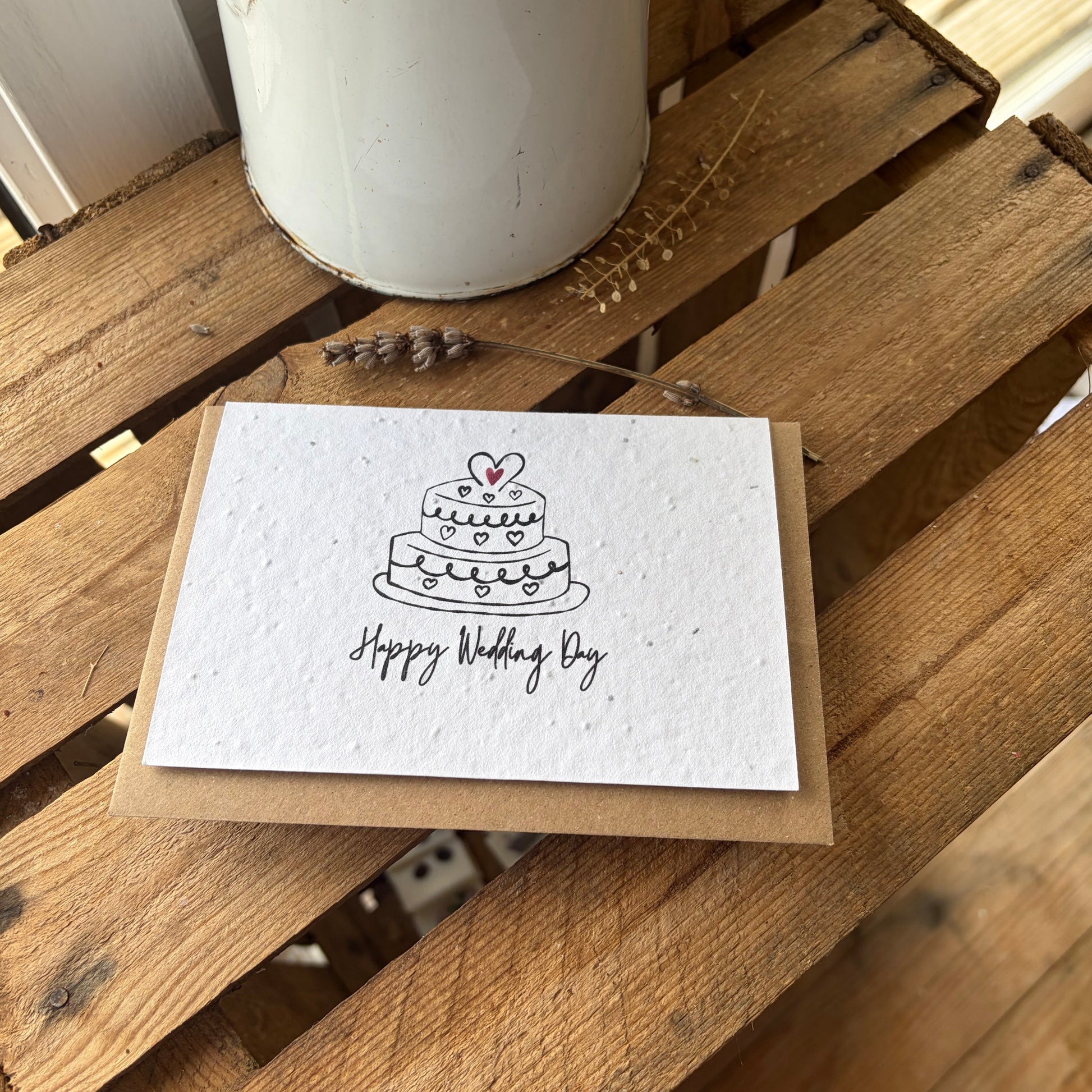 Greeting card with wedding cake illustration and 'Happy Wedding Day' text on a wooden surface.